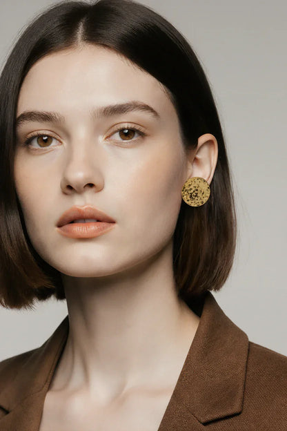Kvinde med kort brunt hår iført stor, rund guldfarvet ørestik og brun blazer, smykke accessories