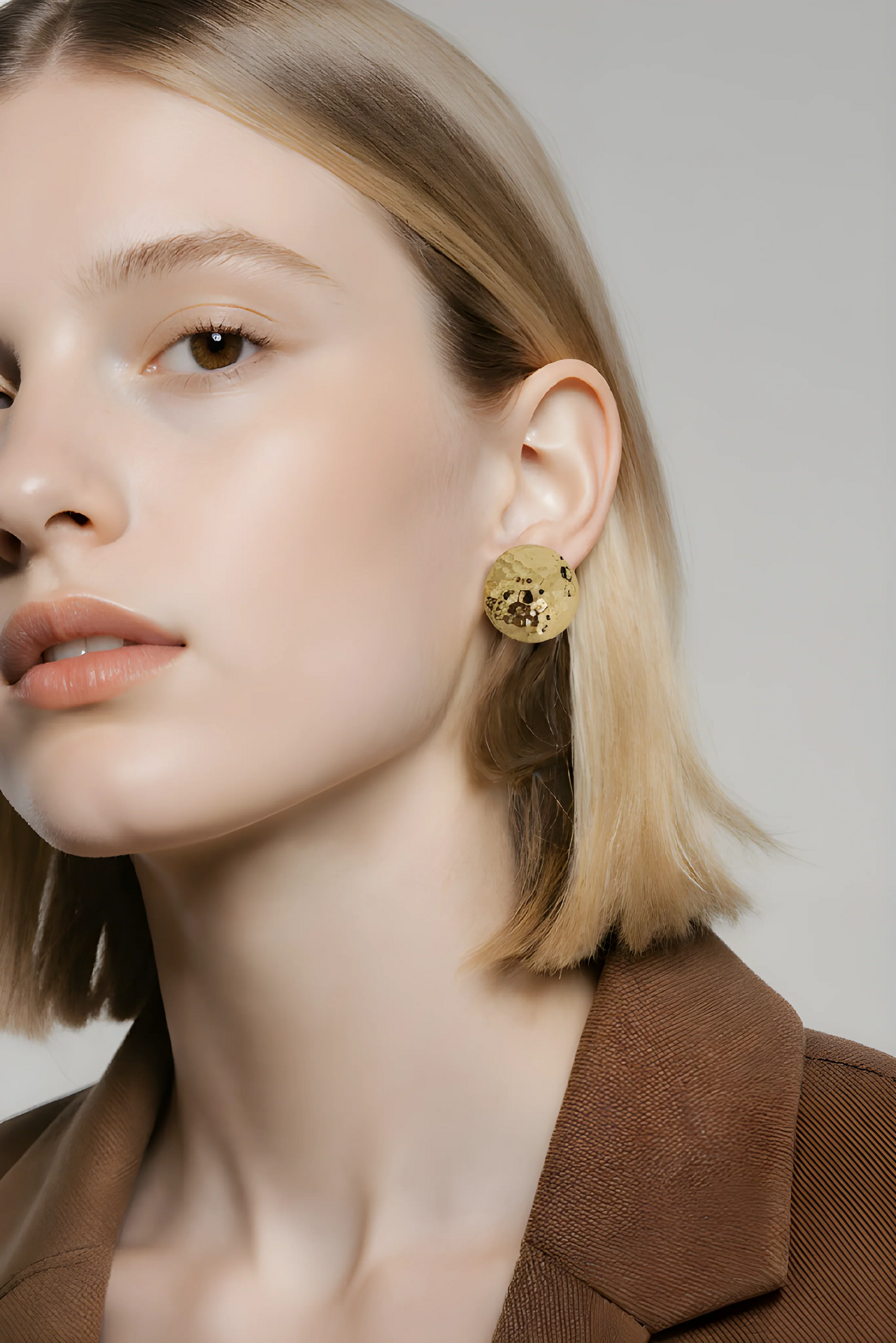Kvinde med kort blondt hår bærer stor, rund, gylden ørering, elegant accessory