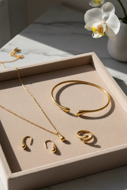 Elegant guld smykkesæt med armbånd, halskæde, øreringe og ring på beige bakke