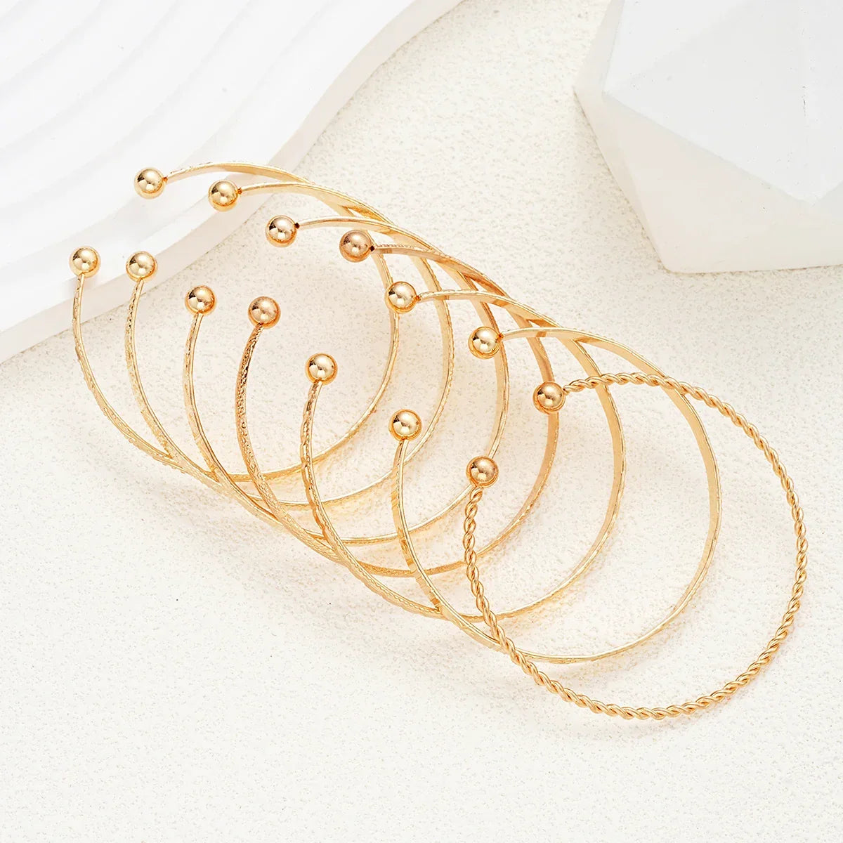 Sæt af elegante gyldne armbånd med kugledetaljer på neutral baggrund, smykker, accessories