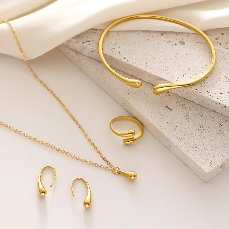 Elegant guld smykke sæt med armbånd, ring, halskæde og ørestikker på lys baggrund