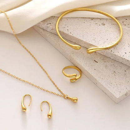 Elegant guld smykke sæt med armbånd, ring, halskæde og ørestikker på lys baggrund