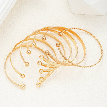 Sæt med elegante guldfarvede armbånd og accessories på lys baggrund, moderne smykker