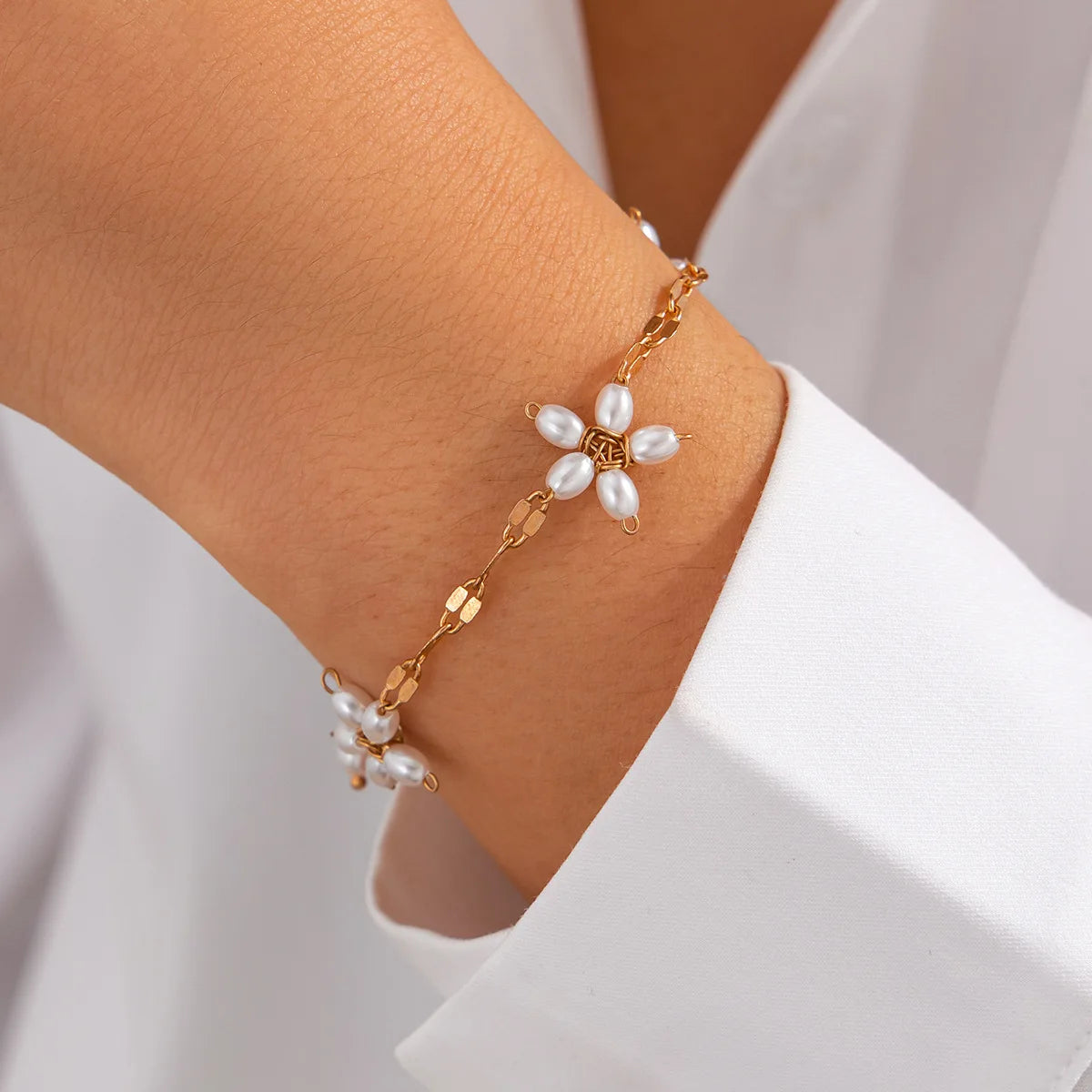 Boho perle armbånd med guldfarvet blomster design og imitationsperler, båret på håndled. Perfekt til boheme-stil fra Stylisk.